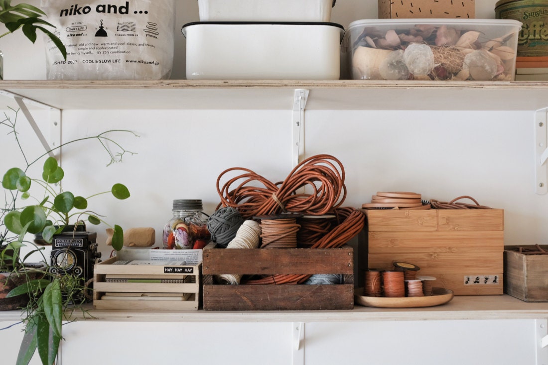 Thread, leather cord, and other supplies organized neatly on the shelves above Quynh's workstation