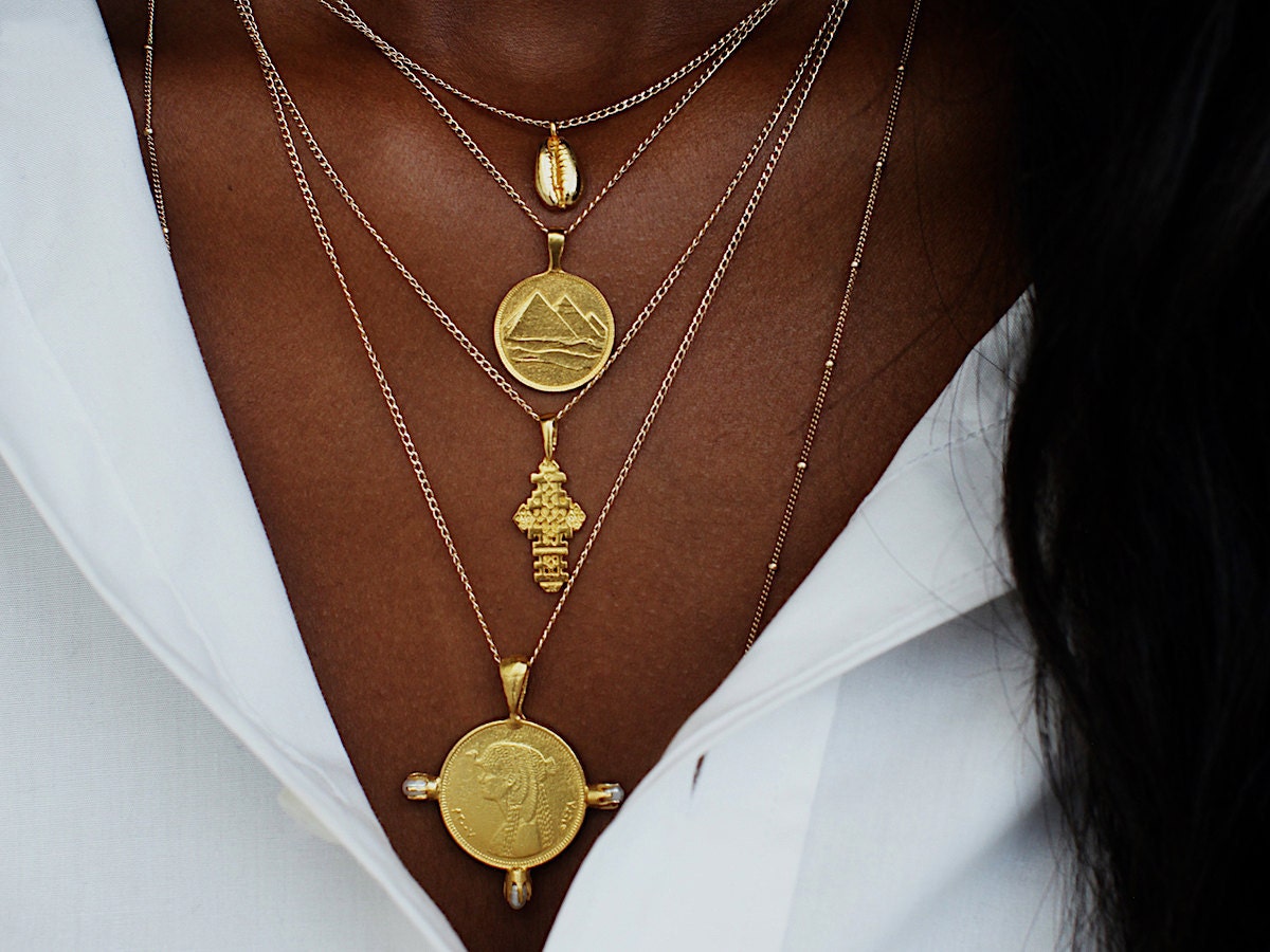 A woman models a stack of gold coin necklaces from Omi Woods