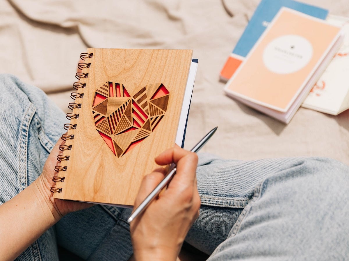 A woman holds a wooden journal decorated with a lasercut heart on the cover from Hereafter