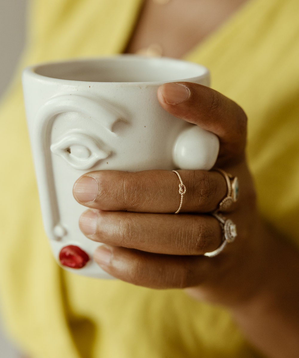 Shay wearing a gold rope knot ring and holding a face cup