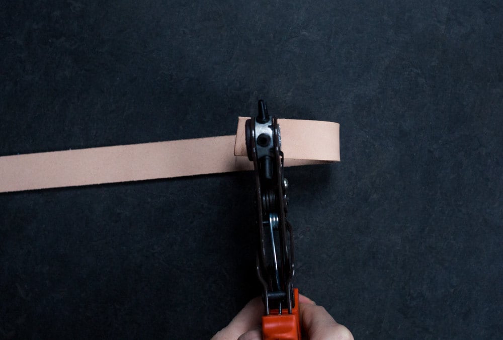 A leather hole punch perforates the strap