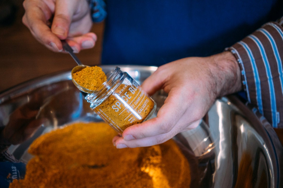 Robert spoons ground curry into a jar.