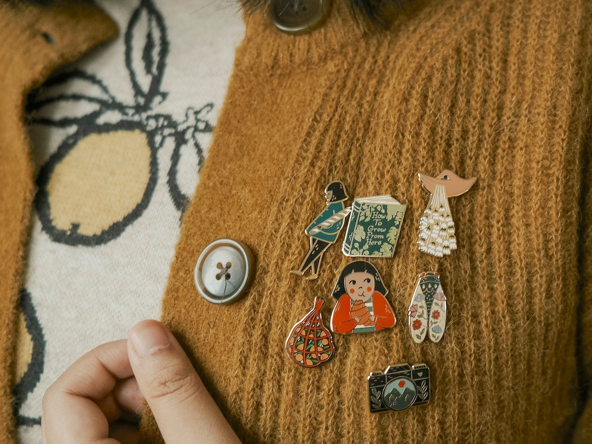 Enamel pins from Justine Gilbuena modeled on a sweater