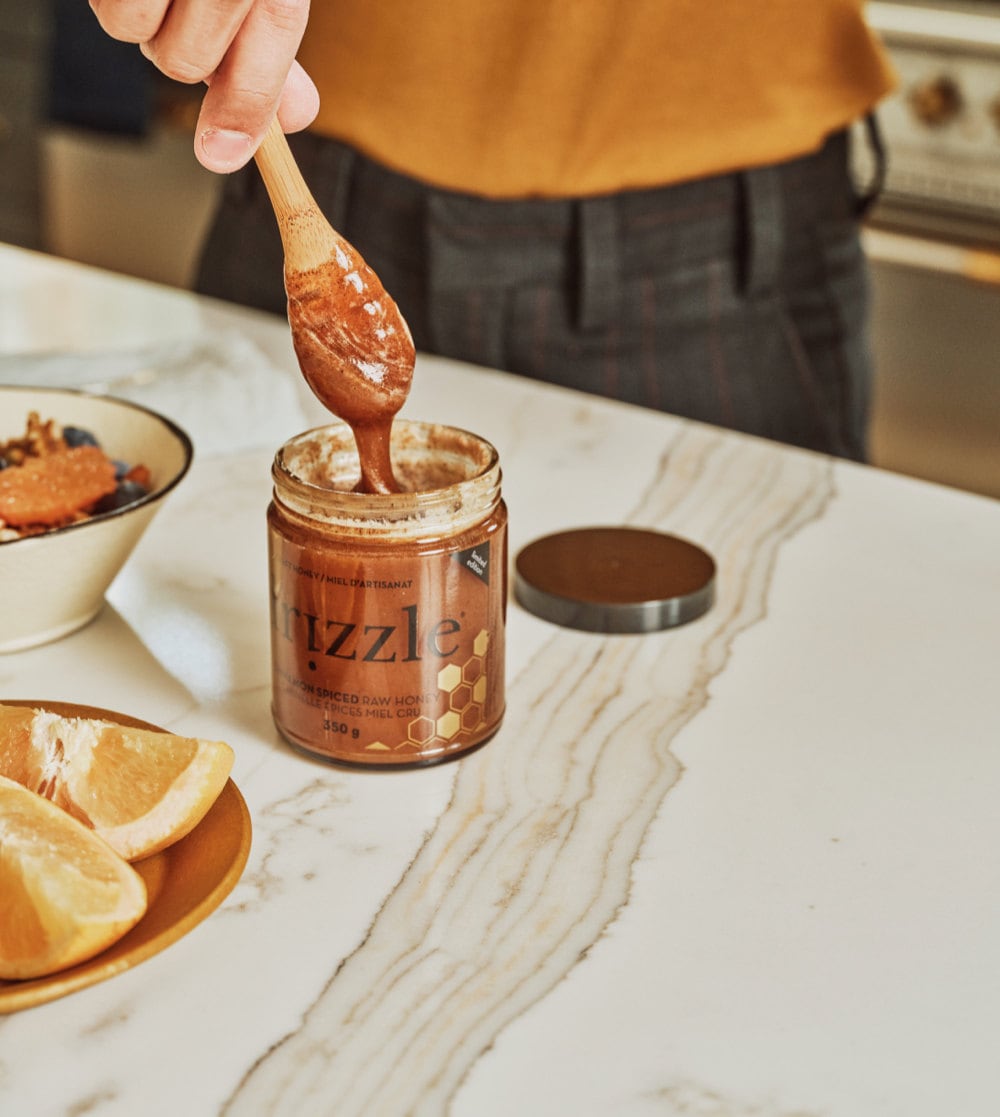 Tan dips a wooden drizzler into a jar of raw Drizzle honey from the Tan France x Etsy collection.