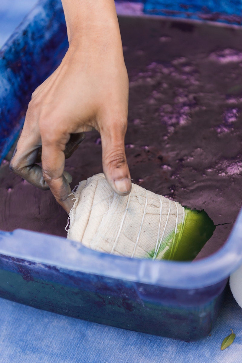 Rajni places a bundle of bound fabric into a vat of dye