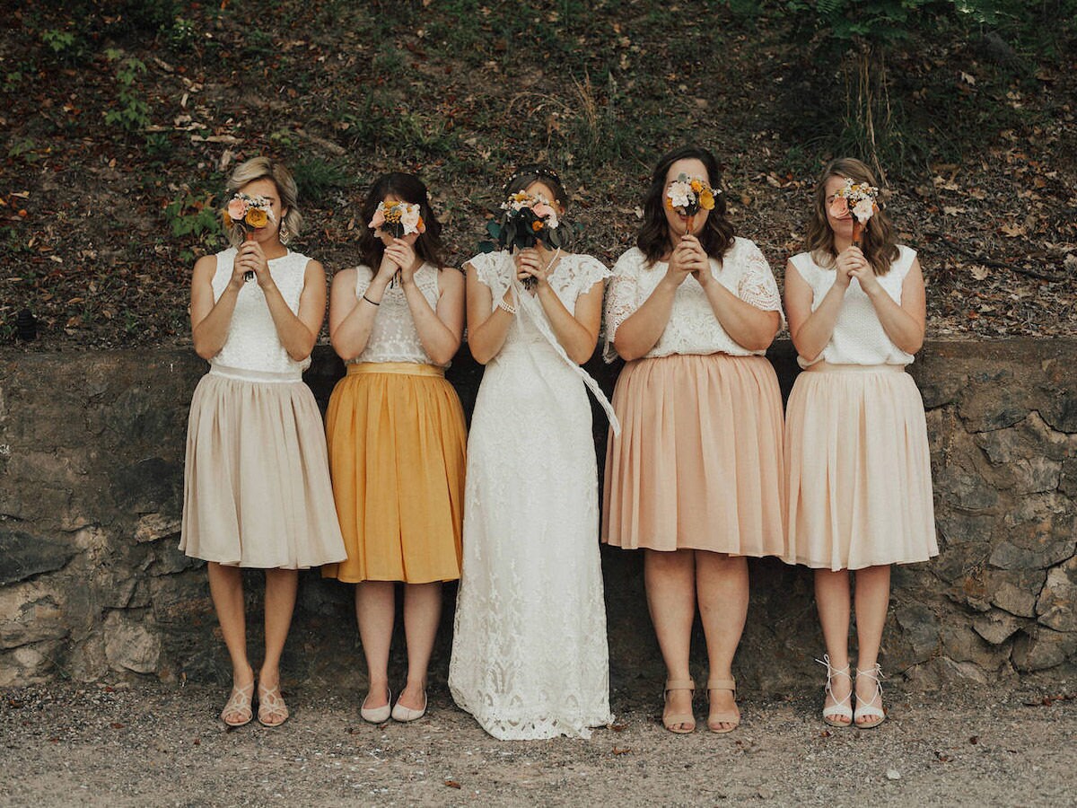 Bridesmaids and bride pose holding bouquets in front of their faces