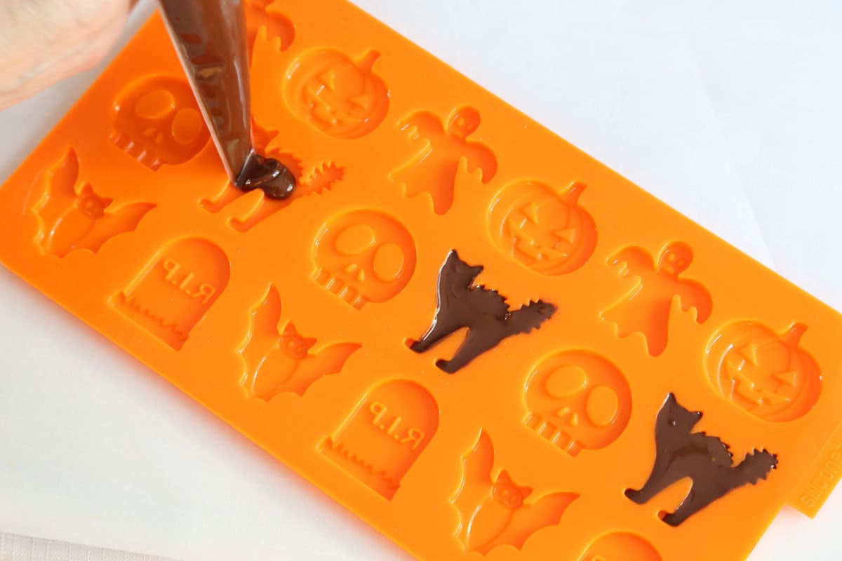 Filling a silicone candy mold with melted chocolate to create candy cats.