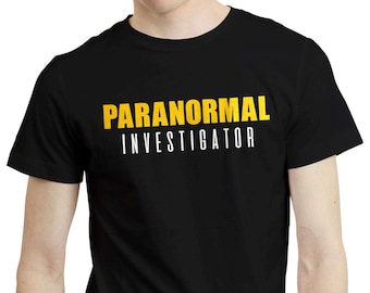 Może przedstawiać: Czarny t-shirt z napisem "PARANORMAL INVESTIGATOR" wydrukowanym w kolorze żółtym i białym. Tekst jest wyśrodkowany na klatce piersiowej. Koszulka ma krótkie rękawy i okrągły dekolt.
