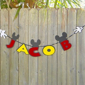 May include: A black and red banner with the name "Jacob" spelled out in large letters. The letters are decorated with Mickey Mouse ears and hands.