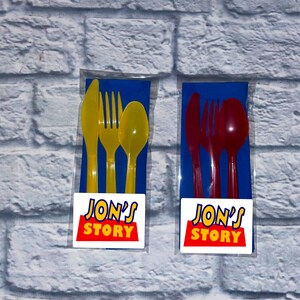 May include: Two sets of plastic cutlery in individual clear plastic bags. The cutlery is yellow and red. Each set includes a knife, fork, and spoon. The bags have a white sticker with the text "JON'S STORY" in red and blue letters.