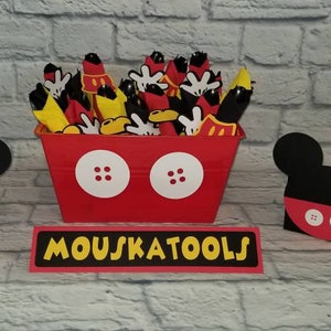 May include: Red and black Mickey Mouse themed party favor containers with black Mickey Mouse ears and red and white buttons. The containers are filled with black plastic utensils. A sign reads "Mouskatools".