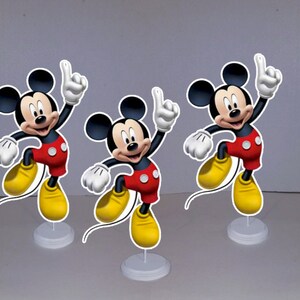 May include: Three Mickey Mouse centerpieces, each featuring a cartoon image of Mickey Mouse in a red and yellow outfit, with a white base.