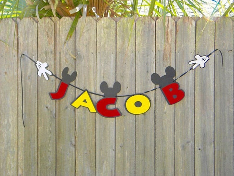 May include: A black and red banner with the name "Jacob" spelled out in large letters. The letters are decorated with Mickey Mouse ears and hands.