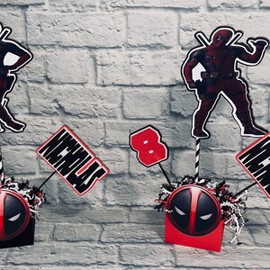 May include: Three red and black Deadpool themed centerpieces with a black and red Deadpool mask, a red number 8, and a white name card that says "Nicholas".