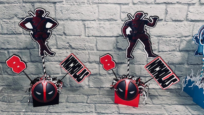 May include: Three red and black Deadpool themed centerpieces with a black and red Deadpool mask, a red number 8, and a white name card that says "Nicholas".