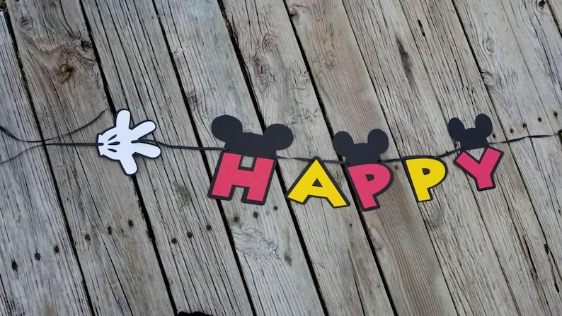 May include: A black, red, and yellow banner with the word "HAPPY" spelled out in large letters. Each letter has a Mickey Mouse head on top. A white Mickey Mouse glove is attached to the left side of the banner.