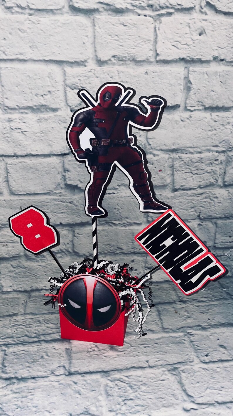 May include: A red and black Deadpool themed centerpiece with a Deadpool figure, a red number 8, and a sign that says "Nicholas".