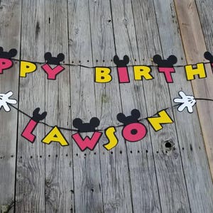 May include: A Mickey Mouse themed birthday banner with black Mickey Mouse ears, red, yellow, and black letters spelling "Happy Birthday Lawson".