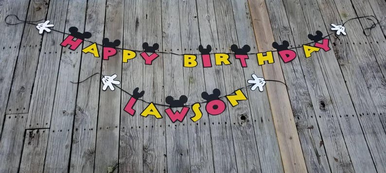 May include: A Mickey Mouse themed birthday banner with black Mickey Mouse ears, red, yellow, and black letters spelling "Happy Birthday Lawson".