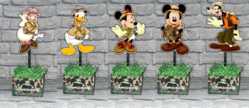 Puede incluir: Cinco centros de mesa con los personajes de Disney Daisy Duck, Donald Duck, Minnie Mouse, Mickey Mouse y Goofy vestidos con ropa de safari. Cada personaje est&aacute; montado en un palo negro en una caja con estampado de leopardo y el nombre CAMDENE.