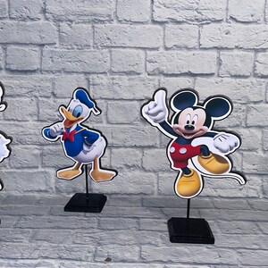 May include: Four cardboard stand-up figures of Disney characters: Mickey Mouse, Minnie Mouse, Donald Duck, and Daisy Duck. The figures are on black stands.