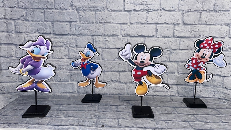 May include: Four cardboard stand-up figures of Disney characters: Mickey Mouse, Minnie Mouse, Donald Duck, and Daisy Duck. The figures are on black stands.