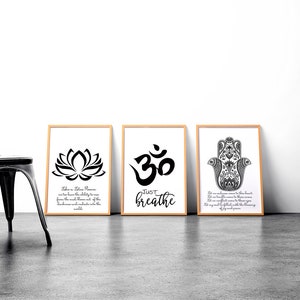 May include: Three framed art prints with a yoga theme. The prints feature a lotus flower, the Om symbol, and a Hamsa hand, all in black and white. The middle print says "Just Breathe". A black metal chair is to the left.