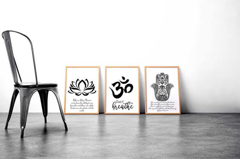 May include: Three framed art prints with a yoga theme. The prints feature a lotus flower, the Om symbol, and a Hamsa hand, all in black and white. The middle print says "Just Breathe". A black metal chair is to the left.