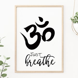 May include: A framed print featuring a black Om symbol and the words "Just breathe" in a cursive font. The artwork is set against a white background, framed in light wood, and suitable for meditation spaces.