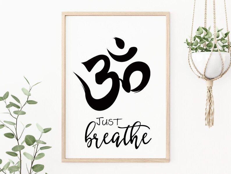 May include: A framed print featuring a black Om symbol and the words "Just breathe" in a cursive font. The artwork is set against a white background, framed in light wood, and suitable for meditation spaces.