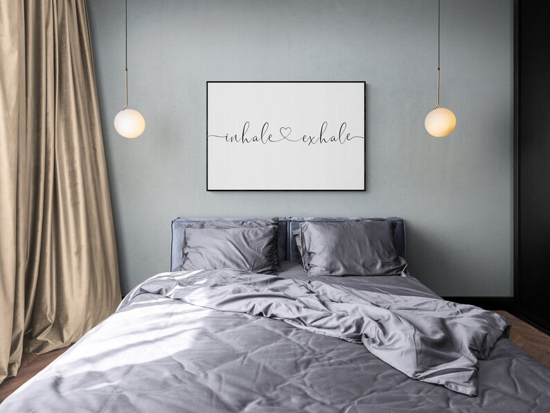 Pu&ograve; includere: Una camera da letto con un letto grigio, biancheria da letto bianca e due lampadari a globo bianco che pendono dal soffitto. Una stampa incorniciata con il testo "inhale exhale" &egrave; appesa al muro sopra il letto.