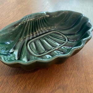 May include: A green ceramic soap dish shaped like a seashell with a raised, ribbed design.