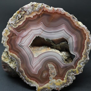 May include: A cross-section of a geode, showcasing concentric bands of color. The interior features a hollow cavity. The rock's layers display shades of brown, white, and purple, with a rough, textured exterior. A natural stone specimen.