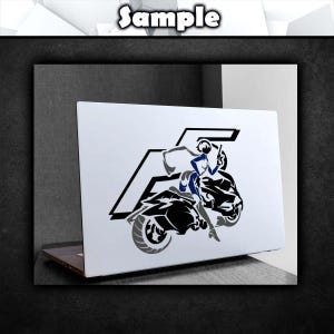 May include: A white laptop with a black and gray decal of a woman riding a motorcycle. The decal has a stylized letter "F" in the background.
