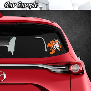 May include: A red car with a white decal of a cartoon character with orange accents on the back window. The character is wearing headphones and holding a weapon.