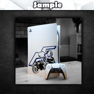 May include: A white PlayStation 5 console with a blue and black decal of a person riding a motorcycle. The console is sitting on a wooden surface next to a white PlayStation 5 controller.
