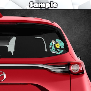 May include: A red car with a rear window sticker featuring a cartoon character in a green and yellow outfit. The character is holding a yellow star and is surrounded by a turquoise circle.