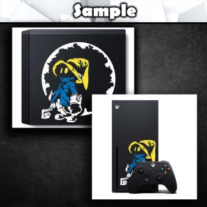 K&ouml;nnte beinhalten: Schwarze Xbox Series X Konsole und Controller mit einem individuellen Grafikdesign eines Cartoon-Charakters in Blau, Gelb und Wei&szlig;. Der Charakter ist vor einem wei&szlig;en, mond&auml;hnlichen Hintergrund platziert.
