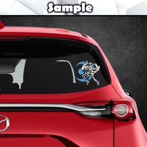 May include: A red car with a rear window sticker featuring a white silhouette of a woman with blue hair and a blue crescent moon.