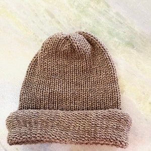 May include: A brown knitted beanie with a ribbed texture. The beanie has a folded brim.