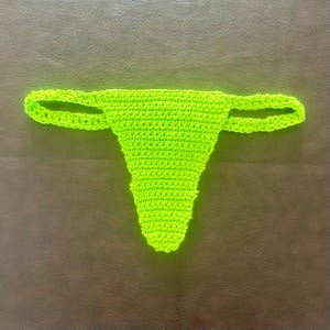 May include: A bright neon green thong crafted from crocheted yarn. The garment features a triangular front panel with a textured stitch pattern and two thin, flexible side straps that connect to the back, creating a simple and functional design.
