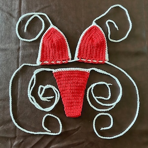 May include: Red crochet bikini top and bottom with white trim. The bikini is laid out on a brown surface with the straps tied in a knot.