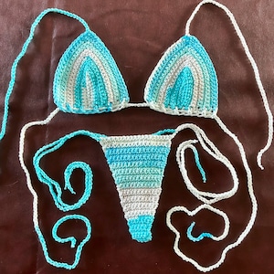 May include: A crocheted bikini set in shades of blue and white. The top is a triangle style with thin straps and the bottom is a cheeky style with ties on the sides.