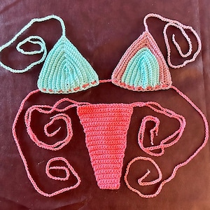 May include: A crocheted bikini set with a pink bottom and a blue and pink top. The bikini is made with a delicate crochet stitch and has a feminine design.