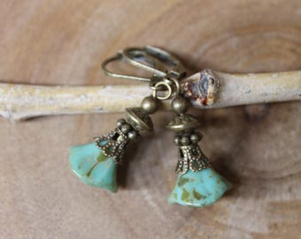 May include: A pair of dangle earrings featuring bell-shaped turquoise glass beads with brown marbling. Each bead is topped with an ornate, antique bronze-colored metal cap and a small bead, attached to a matching bronze-toned lever-back ear wire.