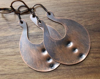 May include: A pair of copper hoop earrings with a hammered texture and a slightly oval shape. The earrings have a rustic, handmade look.