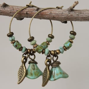May include: A pair of hoop earrings with turquoise and gold beads and leaf charms. The earrings are hanging from a branch.