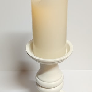 May include: A white pillar candle holder with a white pillar candle with a flickering flame.