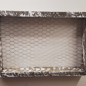 May include: A rustic wooden frame with a whitewashed finish and a wire mesh insert. The frame has a distressed look with chipped paint and exposed wood.