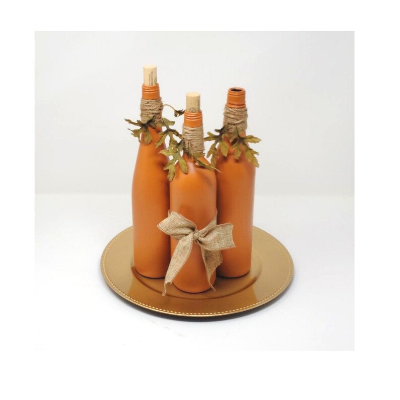Puede incluir: Tres botellas de vidrio naranja con cinta de arpillera y hojas de oto&ntilde;o en un plato dorado.
